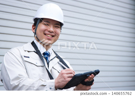 A smiling young man wearing work clothes and a helmet A smiling young man wearing work clothes and a helmet 140655762