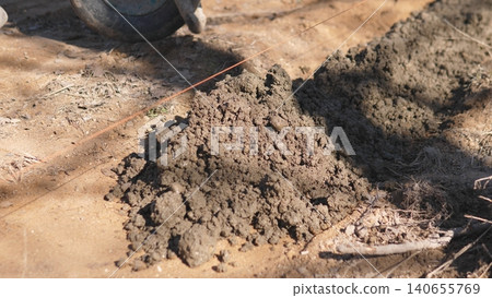 Pile Of Soil And Mortar At Construction Site Ready For Mixing And Leveling, Mound Shows Textured Earth And Aggregate, Nearby Tools And Wheelbarrow Indicate Active Material Supply For Block Pile Of Soil And Mortar At Construction Site Ready For Mixing And Leveling, Mound Shows Textured Earth And Aggregate, Nearby Tools And Wheelbarrow Indicate Active Material Supply For Block 140655769