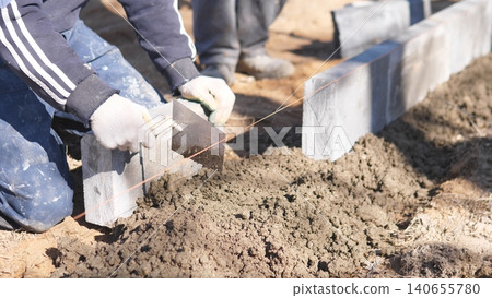 Foundation String Level Check. Stake Cord For Wall Line Accuracy. Crew Uses String To Mark Even Wall Placement. Secured Cord And Stakes Help Ensure Precise Wall Alignment On Sand 140655780