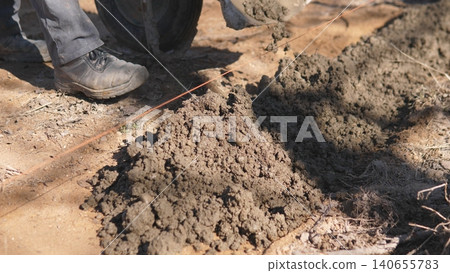 Boots Next To Fresh Mortar Pile On Sandy Site, Showing Work Pause And Gritty Texture Of Building Materials With Nearby Tools And Footprints Indicating Active Masonry Task. Boots Next To Fresh Mortar Pile On Sandy Site, Showing Work Pause And Gritty Texture Of Building Materials With Nearby Tools And Footprints Indicating Active Masonry Task. 140655783