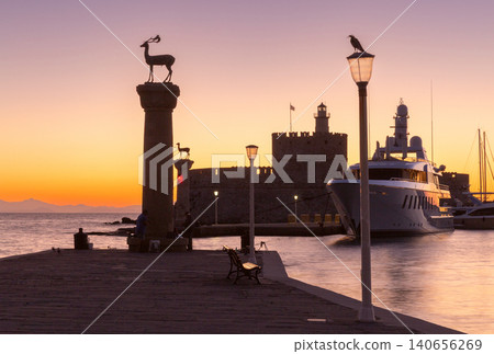 Sunrise view of Mandraki Harbor with Saint Nicholas Fortress, deer monument and luxury yacht in Rhodes, Greece. Sunrise view of Mandraki Harbor with Saint Nicholas Fortress, deer monument and luxury yacht in Rhodes, Greece. 140656269