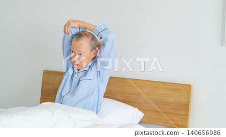 A senior man wakes up in bed and stretches. A senior man wakes up in bed and stretches. 140656986