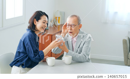 一位老年男子和一位中年女子一邊看著智慧型手機一邊交談。 140657015
