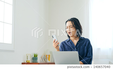 A woman looking disappointed while looking at her smartphone and computer. 140657040