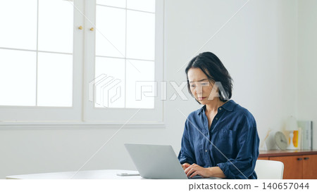 A middle-aged woman is troubled while looking at her computer in her room. A middle-aged woman is troubled while looking at her computer in her room. 140657044