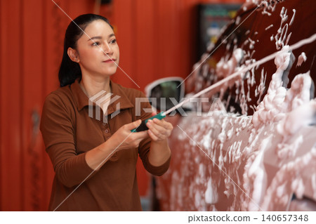 woman washing car with foam in a self-service car wash station woman washing car with foam in a self-service car wash station 140657348