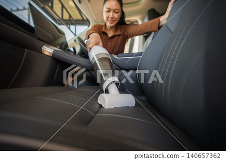 woman using portable handheld vacuum cleaner to clean dust on leather car seat of electric car woman using portable handheld vacuum cleaner to clean dust on leather car seat of electric car 140657362