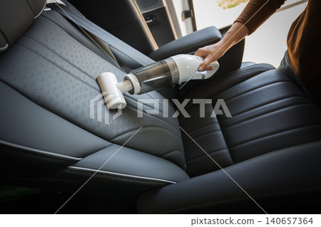 close up hand of woman using portable handheld vacuum cleaner to clean dust on leather car seat of electric car close up hand of woman using portable handheld vacuum cleaner to clean dust on leather car seat of electric car 140657364