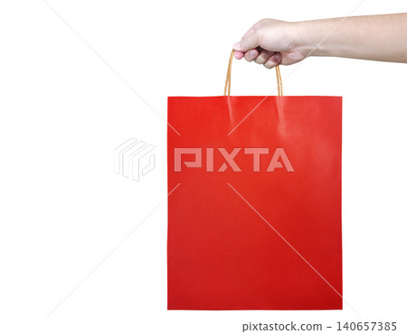 A man's hand is holding a red paper shopping bag against a white background. A man's hand is holding a red paper shopping bag against a white background. 140657385