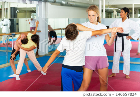 kids in pair exercising self-defense movements during group class with female coach kids in pair exercising self-defense movements during group class with female coach 140657824