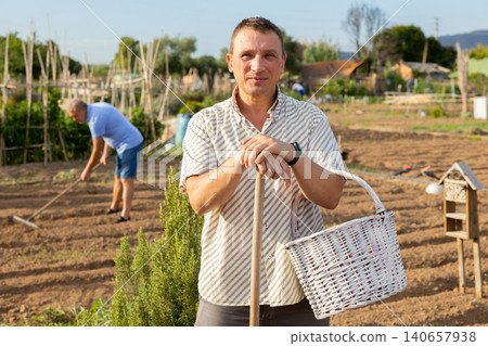 Adult man posing with rake in home vegetable garden Adult man posing with rake in home vegetable garden 140657938