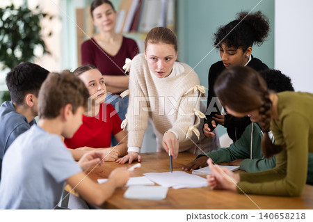 Teenage students solving problem on paper while teacher watches behind Teenage students solving problem on paper while teacher watches behind 140658218