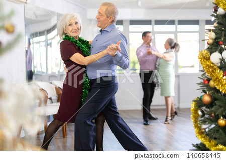 In studio decorated for New Year, elderly couple perky dance pair discofox. Champagne for guests In studio decorated for New Year, elderly couple perky dance pair discofox. Champagne for guests 140658445