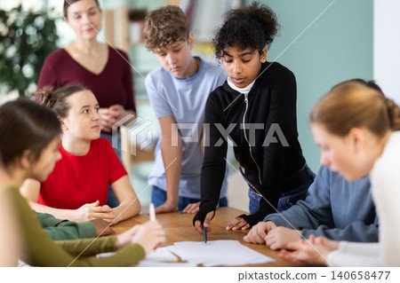 Group of teenagers and students discuss the task at the table in classroom Group of teenagers and students discuss the task at the table in classroom 140658477