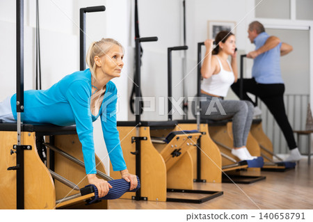 Senior female pensioner training hands and lower back while laying on Pilates Wanda chair in rehabilitation center 140658791