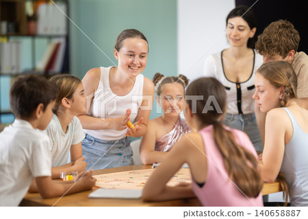 Children and teenagers playing board game at table with teacher nearby Children and teenagers playing board game at table with teacher nearby 140658887