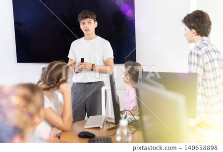 Young computer science teacher standing near an interactive whiteboard tells new material to teenage students in school computer class 140658898