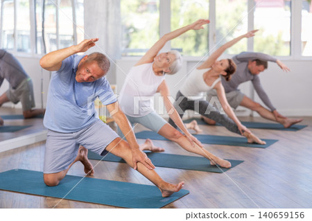 Athletic mature women and men doing side bend, effective pose for back flexibility in group training Athletic mature women and men doing side bend, effective pose for back flexibility in group training 140659156