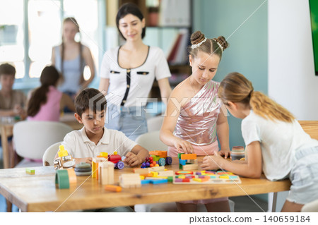 Preteen children playing with wooden construction blocks monitored by teacher Preteen children playing with wooden construction blocks monitored by teacher 140659184