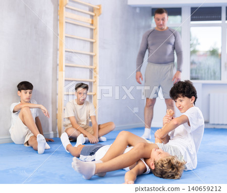 Two young boys training joint lock movement during group karate training. Their teacher standing behind and observing Two young boys training joint lock movement during group karate training. Their teacher standing behind and observing 140659212
