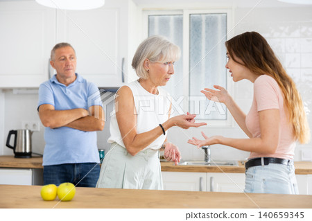 Quarrel between an elderly mother and an adult daughter in home kitchen. Father tries to calm everyone Quarrel between an elderly mother and an adult daughter in home kitchen. Father tries to calm everyone 140659345