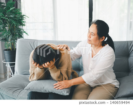 Caring Asian woman comforting a sad young woman on a sofa with a pillow, showing family support, empathy, stress relief, reassurance, mental wellness, home care, and emotional healing. Caring Asian woman comforting a sad young woman on a sofa with a pillow, showing family support, empathy, stress relief, reassurance, mental wellness, home care, and emotional healing. 140659494