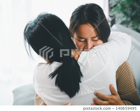Close-up of an Asian woman hugging a young woman at home, showing comfort, forgiveness, family love, emotional healing, empathy, support, trust, reconciliation, and mental wellness care concept. Close-up of an Asian woman hugging a young woman at home, showing comfort, forgiveness, family love, emotional healing, empathy, support, trust, reconciliation, and mental wellness care concept. 140659495