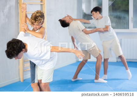 Concentrated preteen boys practicing effective self defence techniques with coach in training room Concentrated preteen boys practicing effective self defence techniques with coach in training room 140659518