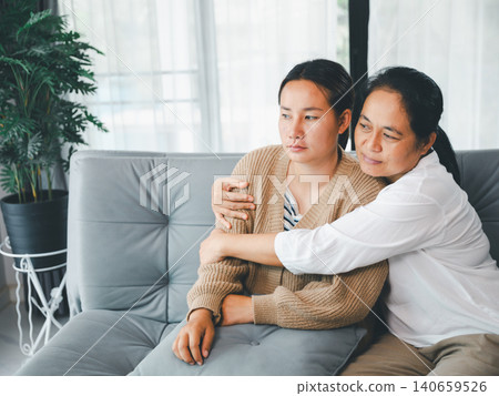 Asian caregiver hugging a young woman in a cozy home living room, showing family support, empathy, emotional healing, comfort, reassurance, trust, bonding, and mental wellness care scene. Asian caregiver hugging a young woman in a cozy home living room, showing family support, empathy, emotional healing, comfort, reassurance, trust, bonding, and mental wellness care scene. 140659526