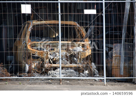 Completely destroyed car wreck behind a metal fence after a fire Completely destroyed car wreck behind a metal fence after a fire 140659596