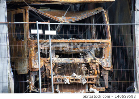 Burnt And Rusted Truck Cab Behind Safety Fence Showing Fire Damage And Urban Wreckage Burnt And Rusted Truck Cab Behind Safety Fence Showing Fire Damage And Urban Wreckage 140659598