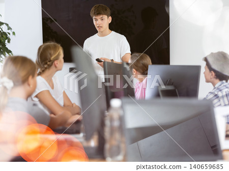 Friendly young teacher standing near an interactive whiteboard telling new material to teenage students in school computer class 140659685