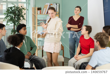 Teenage girl talking to students sitting in circle while teacher watching 140659767