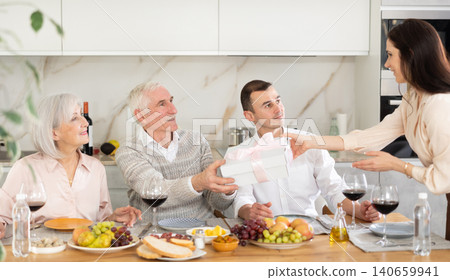 Daughter-in-law presenting birthday gift to elderly father-in-law at family celebration Daughter-in-law presenting birthday gift to elderly father-in-law at family celebration 140659941