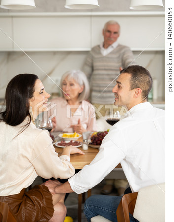 Young couple flirting sitting around table together with old family members looking with objection Young couple flirting sitting around table together with old family members looking with objection 140660053
