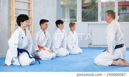 Preteen students and trainer in kimono sitting in seiza pose in sports hall 140660067