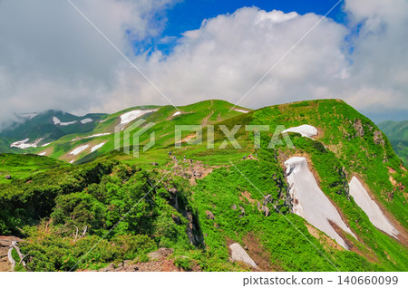 A clear blue sky after the end of the rainy season, with rising clouds and the green slopes and remaining snow of Mount Chokai. 140660099