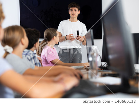 Guy teacher teaches group of students in computer class Guy teacher teaches group of students in computer class 140660138