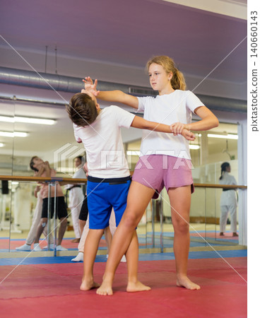 Kids in pair exercising self-defense movements during group class with female coach 140660143