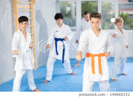 Teenager in kimono practicing punches during group martial arts workout Teenager in kimono practicing punches during group martial arts workout 140660152