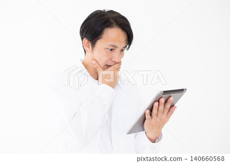 一位身穿白襯衫的中年男子在白色背景前,一臉驚訝地看著平板電腦。 一位身穿白襯衫的中年男子在白色背景前,一臉驚訝地看著平板電腦。 140660568