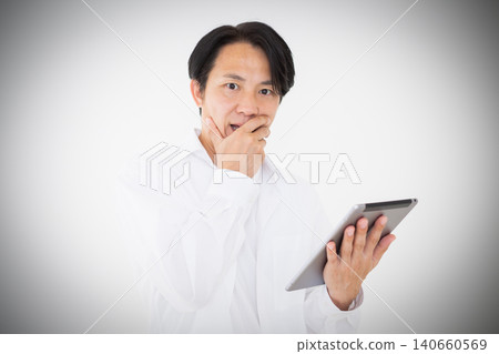 Portrait of a middle-aged man in a white shirt looking surprised at a tablet, against a white background. Portrait of a middle-aged man in a white shirt looking surprised at a tablet, against a white background. 140660569