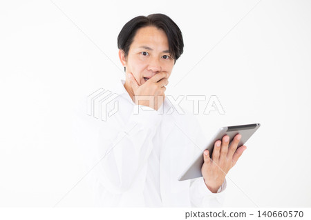 一位身穿白襯衫的中年男子在白色背景前,一臉驚訝地看著平板電腦。 一位身穿白襯衫的中年男子在白色背景前,一臉驚訝地看著平板電腦。 140660570