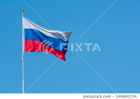 Russian tricolor flag waving in the wind against a blue sky. Fieldbird sits on a branch in spring with a blurred background. Russian tricolor flag waving in the wind against a blue sky. Fieldbird sits on a branch in spring with a blurred background. 140660724