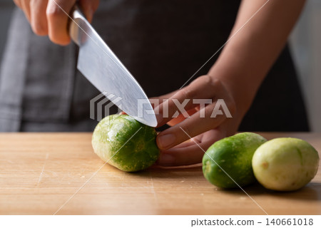 Woman hand holding knife and cutting fresh cucumber on wooden board for homemade cooking Woman hand holding knife and cutting fresh cucumber on wooden board for homemade cooking 140661018