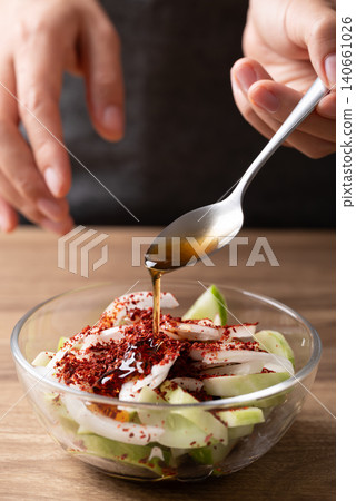 Woman hand pouring sesame oil into a bowl with cucumber to making cucumber salad Woman hand pouring sesame oil into a bowl with cucumber to making cucumber salad 140661026