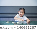 Young girl engaging with dough or clay at a modern kitchen countertop, focused on shaping or arranging circular objects with a calm and concentrated expression 140661267