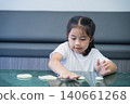 Young Girl Enjoying Playful Activity with Dough, Sitting at Table in Bright Classroom Environment, Engaging in Creative and Educational Hands-On Learning 140661268
