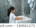 Young girl washing her hands in a modern bathroom with grey marble tiles, mirror, and hairdryer, demonstrating hygiene and personal care routines 140661272