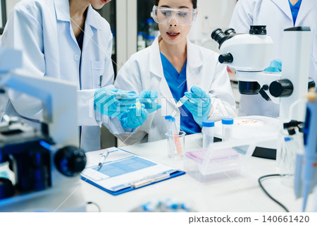 Team of scientists analyzing blue liquid samples in a modern lab, showcasing biotechnology, chemistry, and medical research Team of scientists analyzing blue liquid samples in a modern lab, showcasing biotechnology, chemistry, and medical research 140661420
